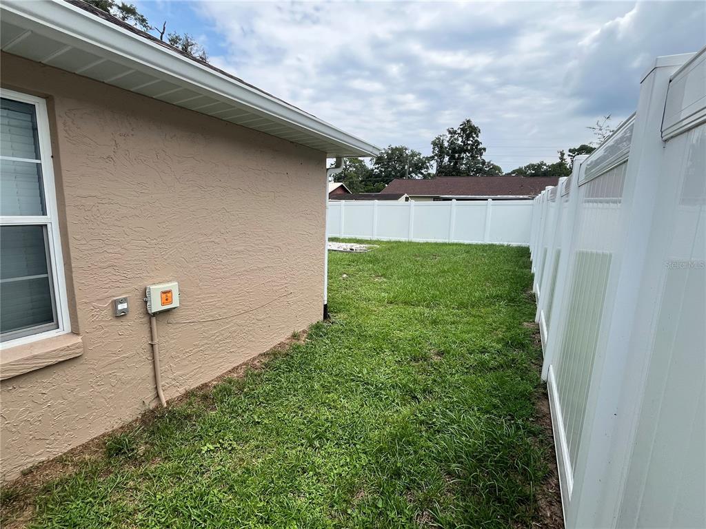 A side yard features a tan house wall, a white vinyl fence, and grass — 3201 NE 42ND PLACE, OCALA, FL