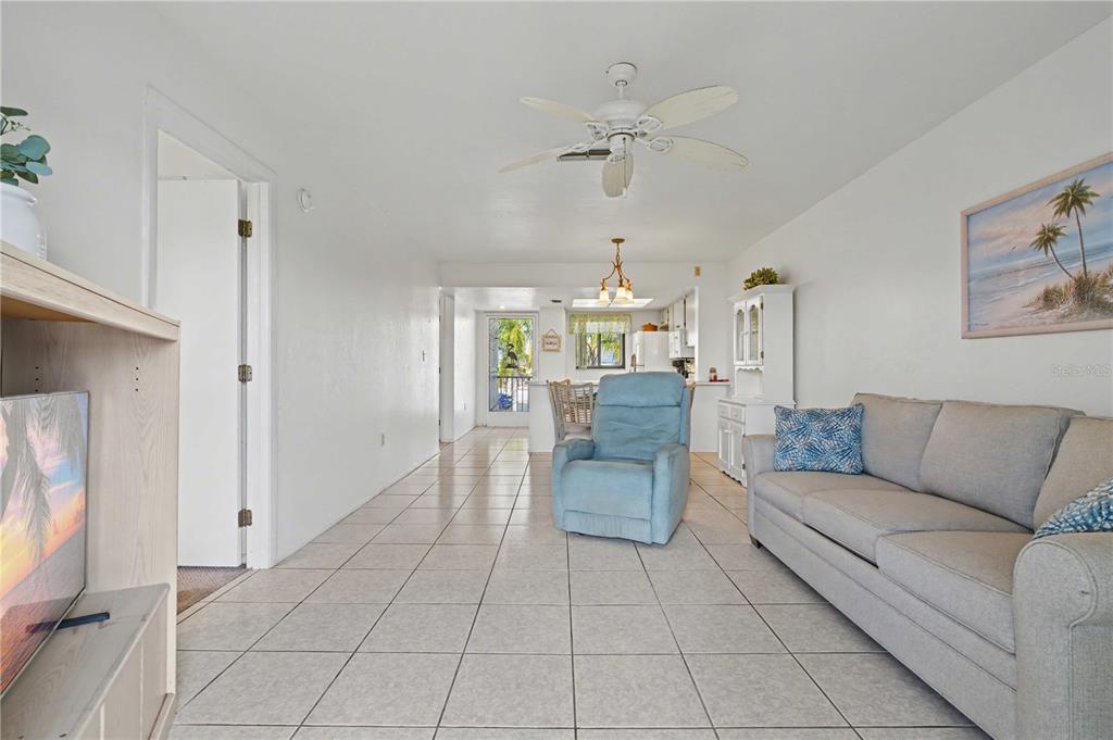 A living room features light tile flooring, a grey sofa, a blue recliner, and ceiling fan — 25225 RAMPART BOULEVARD UNIT 1606, PUNTA GORDA, FL