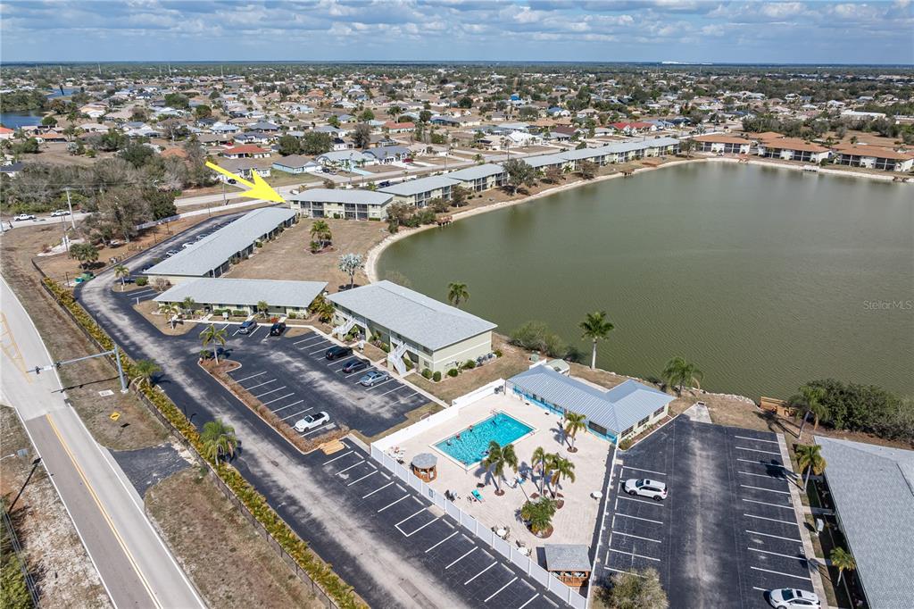 An aerial view shows apartment buildings, a swimming pool, and a lake — 25225 RAMPART BOULEVARD UNIT 1606, PUNTA GORDA, FL