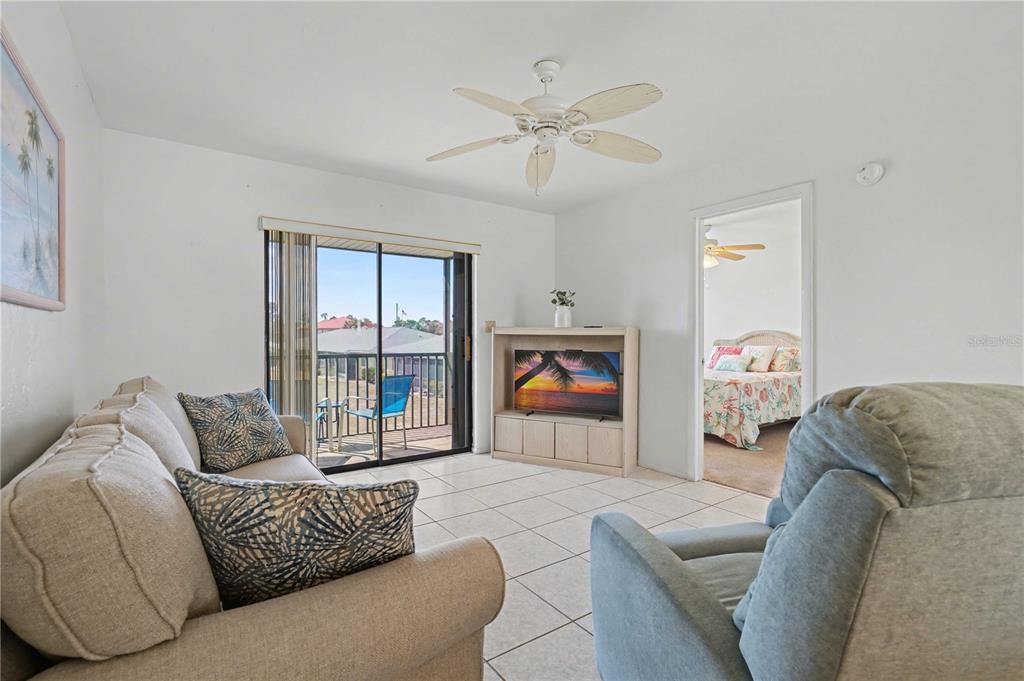 A living room with tile floors, a ceiling fan, a sofa, and a balcony view — 25225 RAMPART BOULEVARD UNIT 1606, PUNTA GORDA, FL