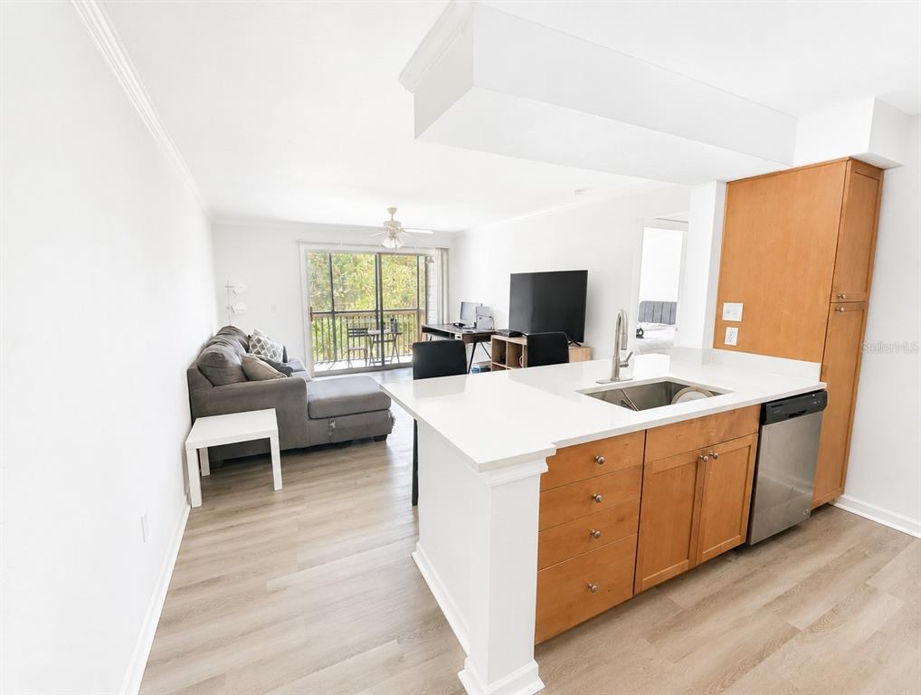 A kitchen with light wood cabinets and white countertops opens into a living area — 2500 WINDING CREEK BOULEVARD UNIT E208, CLEARWATER, FL