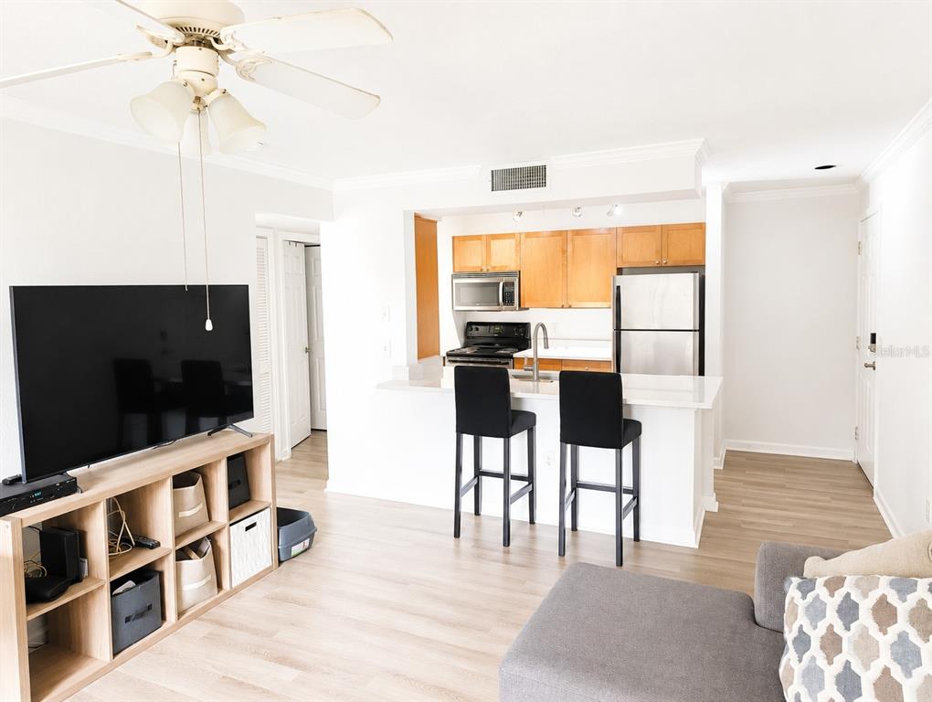 A living room with a television console, breakfast bar, and open kitchen with wood cabinets — 2500 WINDING CREEK BOULEVARD UNIT E208, CLEARWATER, FL