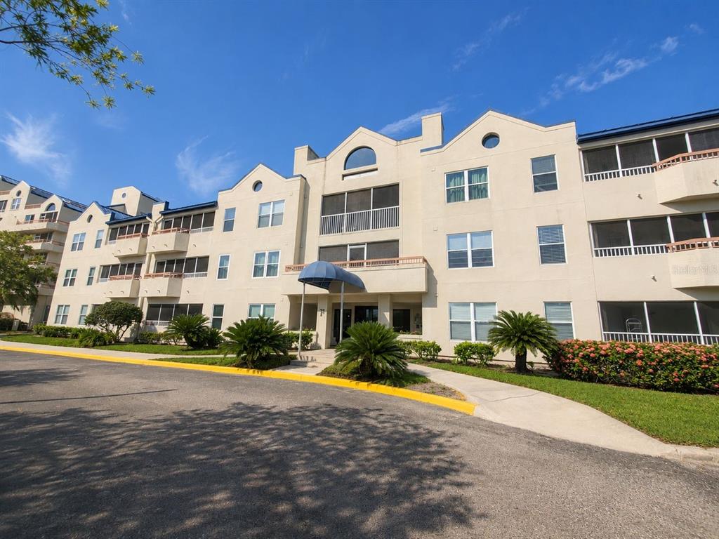 A multi-story beige apartment building with screened balconies and a blue awning entrance — 2323 FEATHER SOUND DRIVE UNIT 205, CLEARWATER, FL