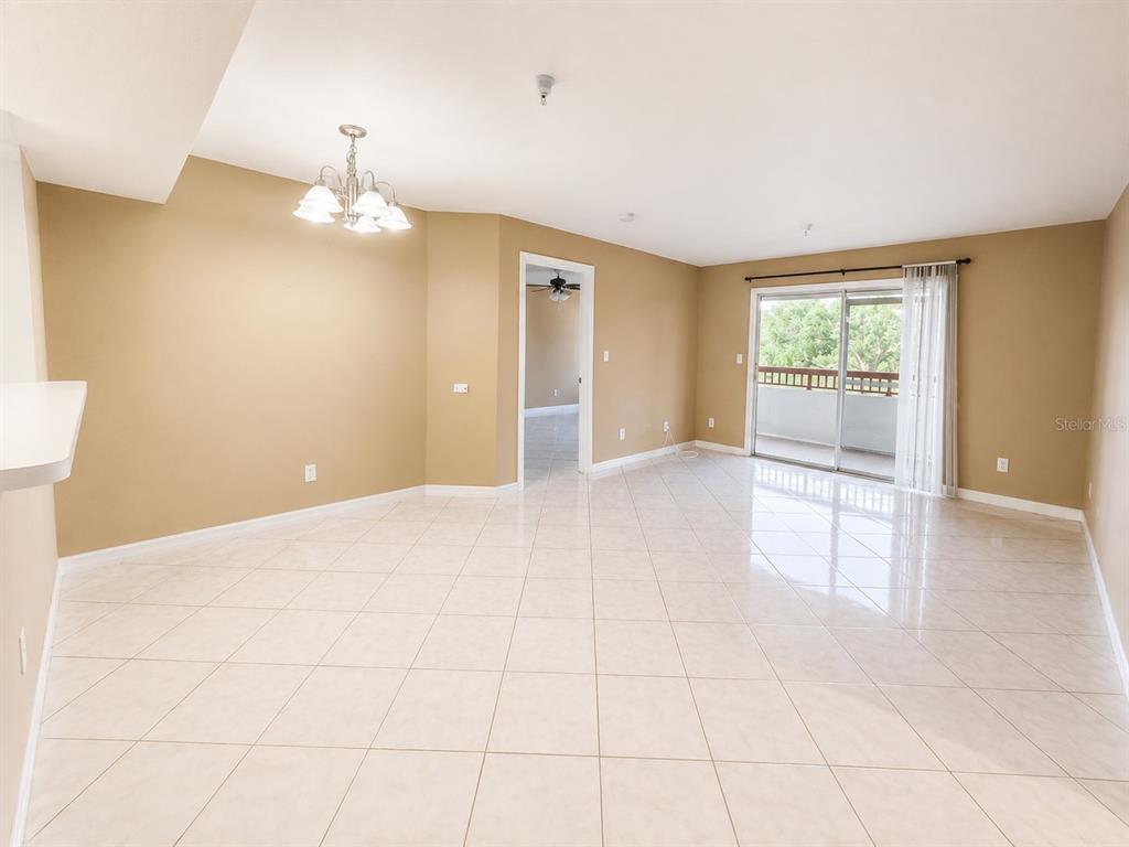 An empty living room with beige walls, tile flooring, a chandelier, and sliding glass doors — 2323 FEATHER SOUND DRIVE UNIT 205, CLEARWATER, FL