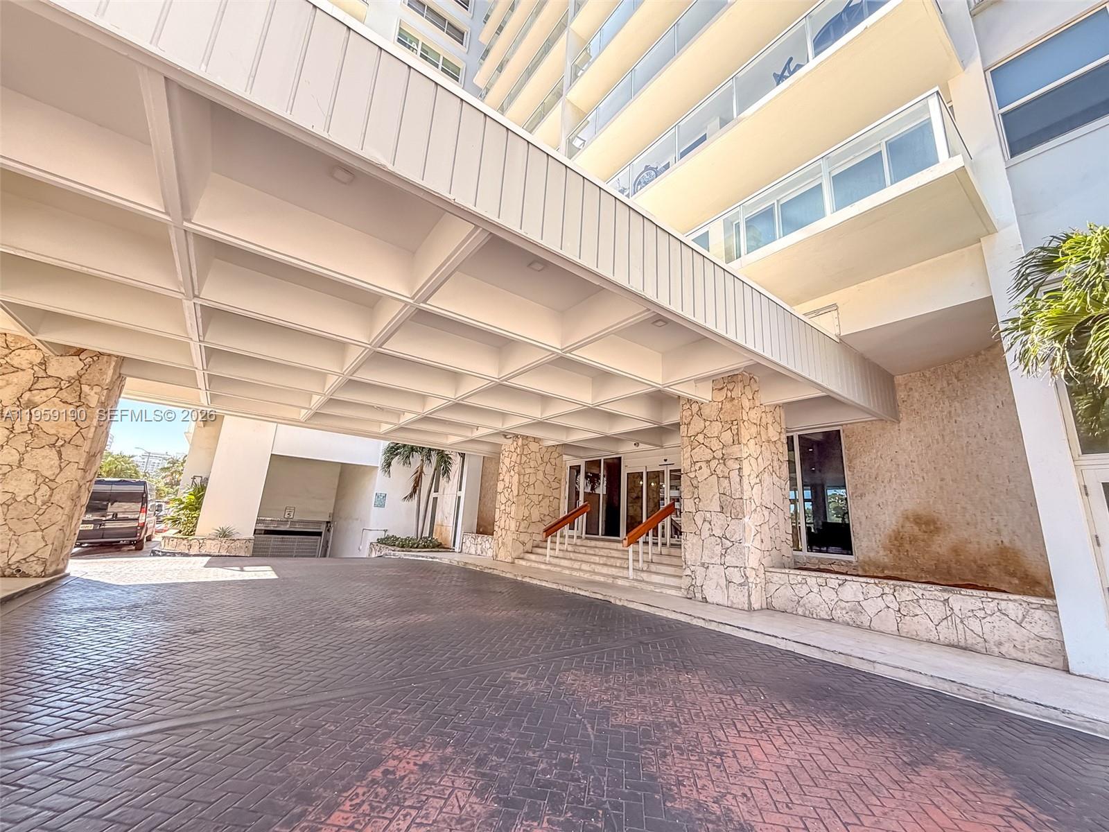 The exterior of a multi-story building features a large covered driveway with stone pillars — 5750 Collins Ave # 6J, Miami Beach FL 33140, MIAMI BEACH, FL