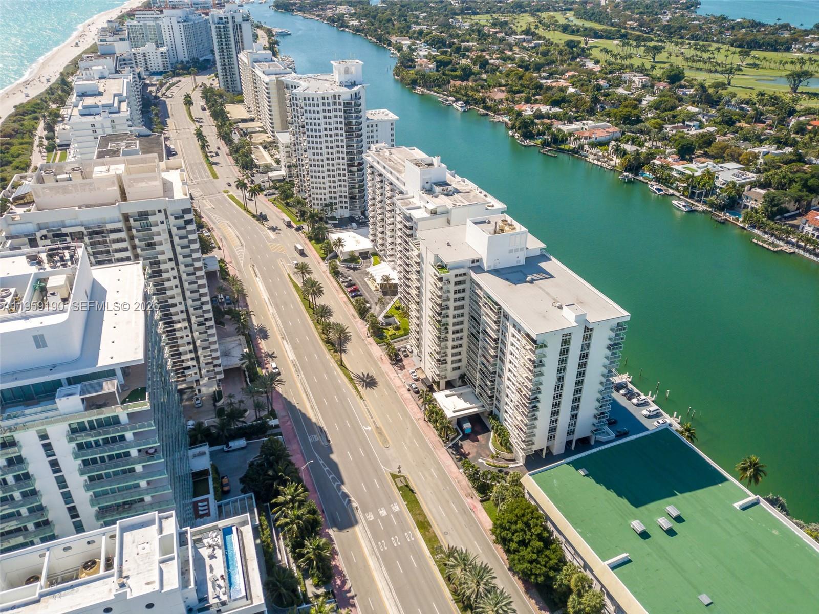 An aerial view shows high-rise apartment buildings along a coastal road and a waterway — 5750 Collins Ave # 6J, Miami Beach FL 33140, MIAMI BEACH, FL