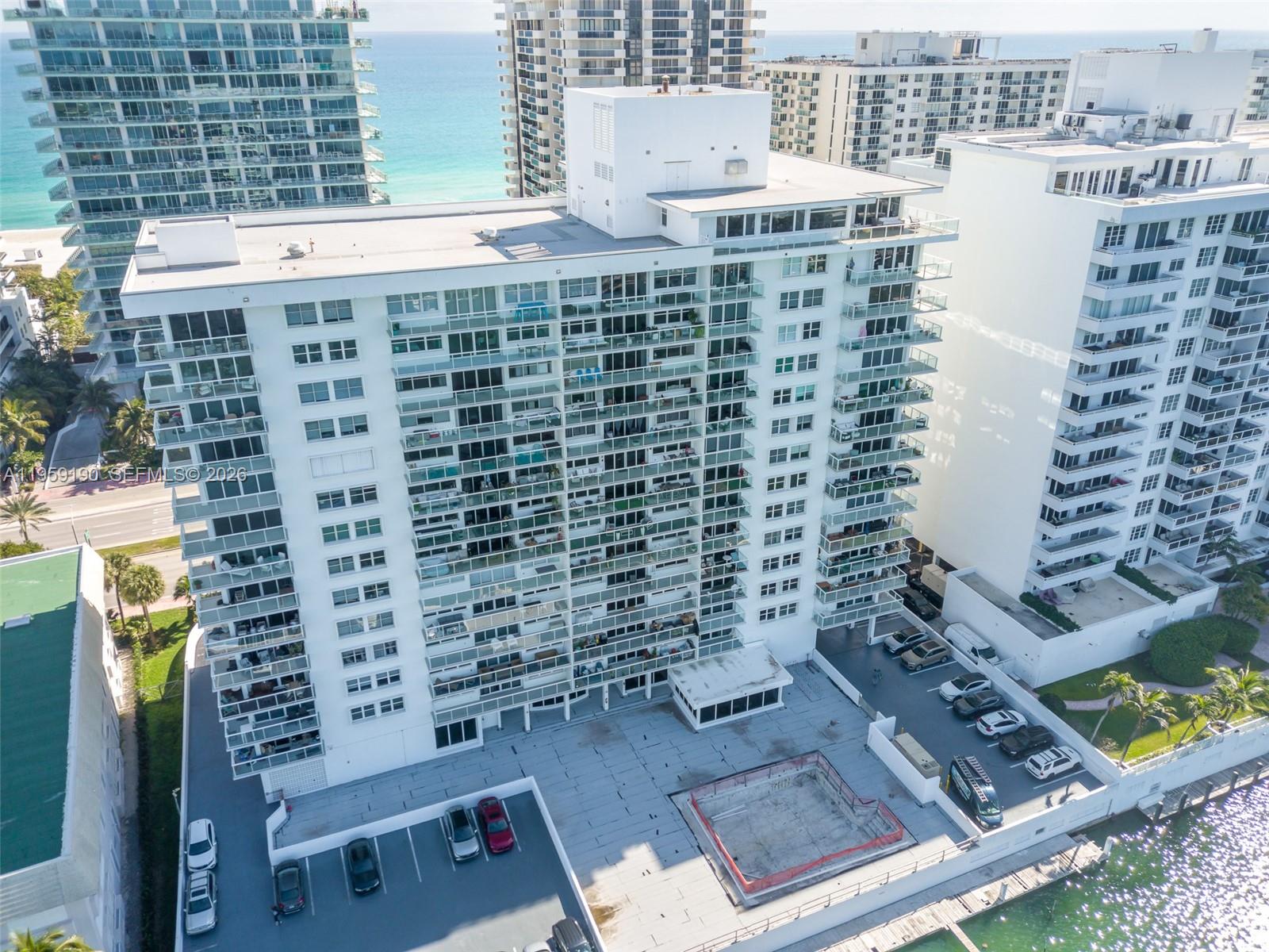 An aerial view shows a white multi-story residential building with balconies and a parking lot — 5750 Collins Ave # 6J, Miami Beach FL 33140, MIAMI BEACH, FL