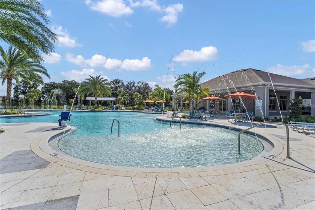 A swimming pool with a fountain feature and lounge chairs sits outside a community building — 1817 WALNUT CREEK DRIVE, KISSIMMEE, FL