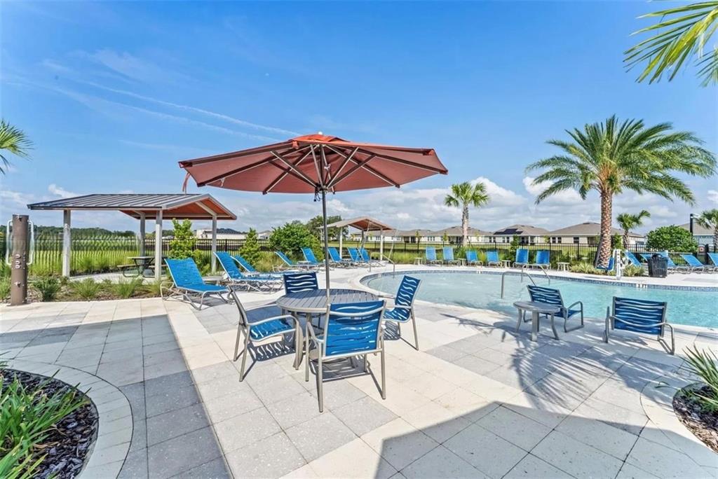 A swimming pool area features lounge chairs, a patio table with an umbrella, and palm trees — 1817 WALNUT CREEK DRIVE, KISSIMMEE, FL