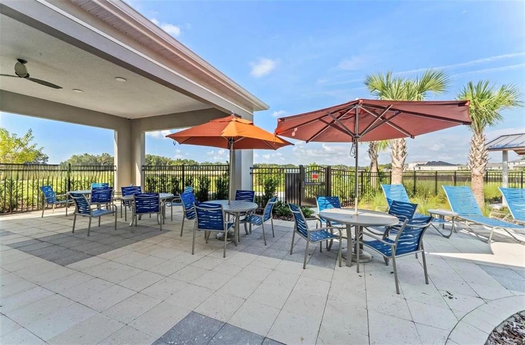 A paved outdoor patio features dining tables with umbrellas, blue chairs, and lounge seating — 1817 WALNUT CREEK DRIVE, KISSIMMEE, FL