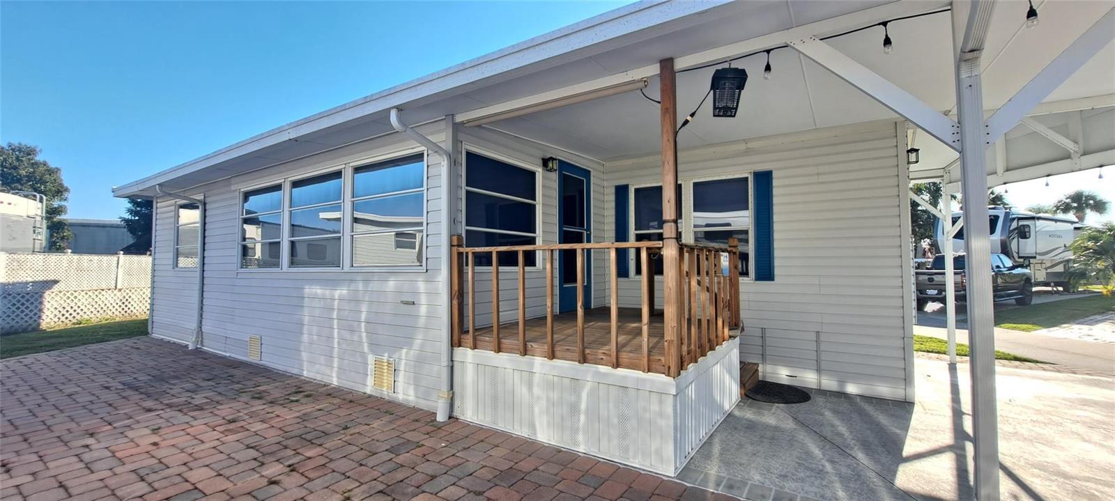 A mobile home exterior features a wooden porch, white siding, and a brick patio area — 5362 SE 65th Avenue, Okeechobee FL 34974, OKEECHOBEE, FL
