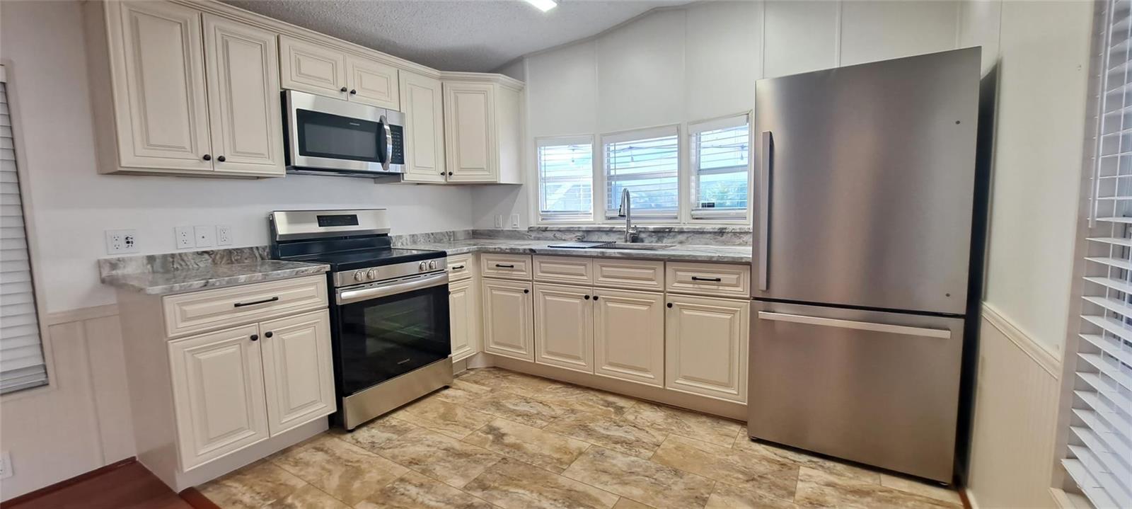 A kitchen features cream-colored cabinets, stainless steel appliances, and marble-patterned countertops — 5362 SE 65th Avenue, Okeechobee FL 34974, OKEECHOBEE, FL