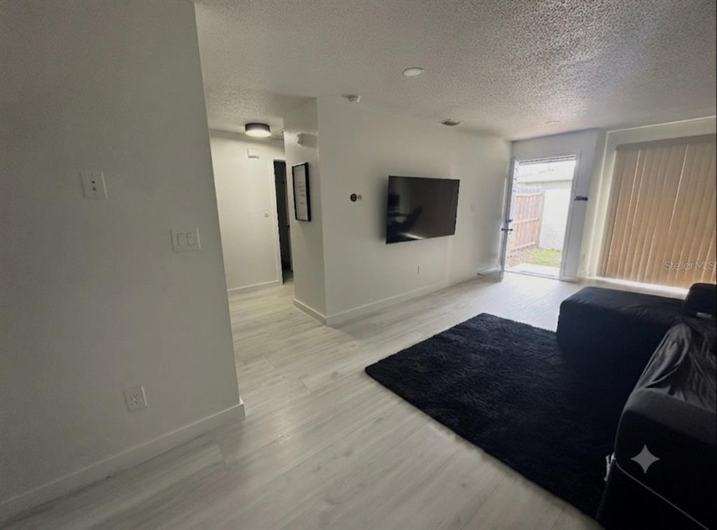 A living room with light wood-look flooring, a wall-mounted television, and a sliding glass door — 5355 SE 29TH PLACE, OCALA, FL