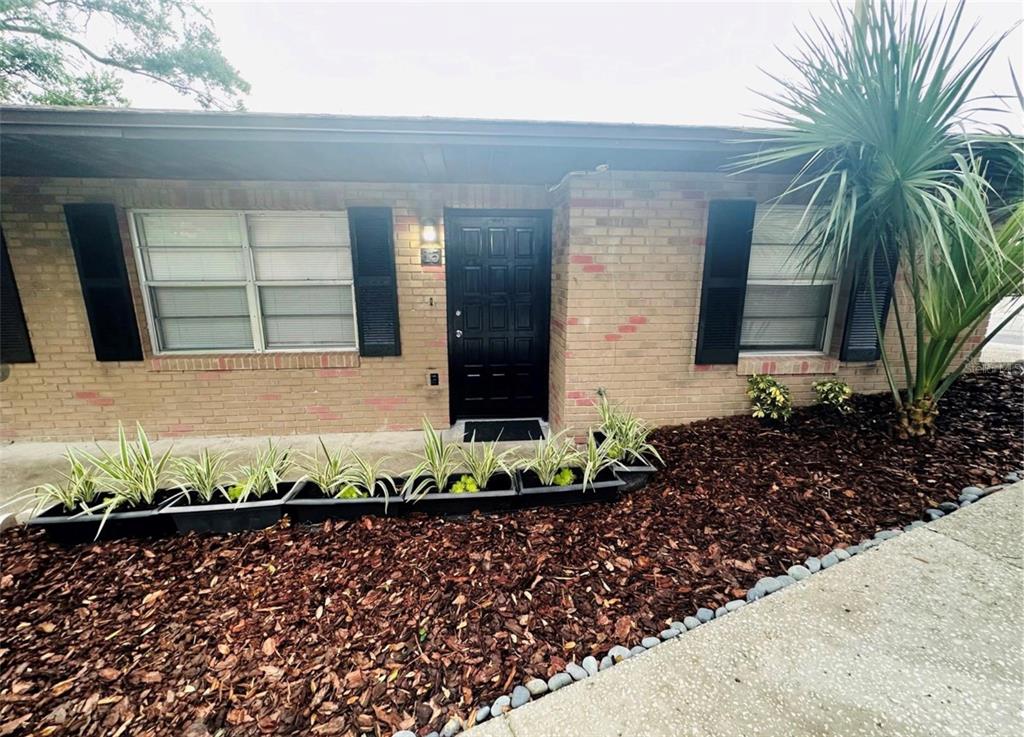 A single-story brick house features a black front door, dark shutters, and a mulched garden — 101 LAKE HUNTER DRIVE UNIT 15 & 16, LAKELAND, FL