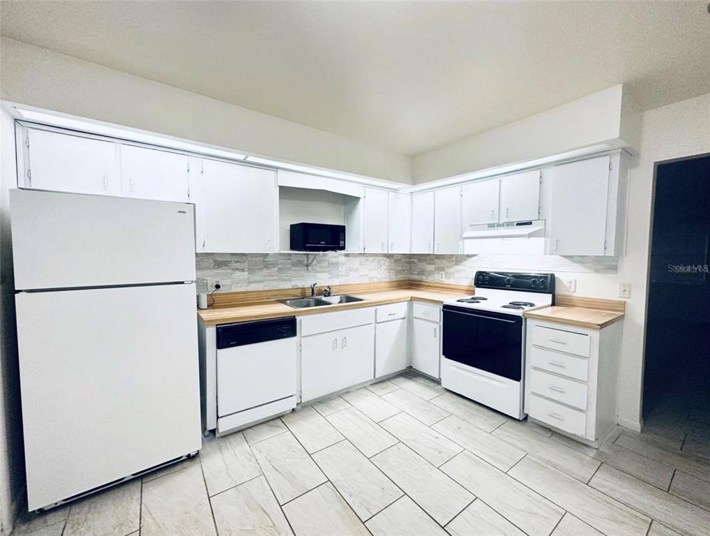 A kitchen with white cabinets, light wood countertops, white appliances, and light-colored tile flooring — 101 LAKE HUNTER DRIVE UNIT 15 & 16, LAKELAND, FL
