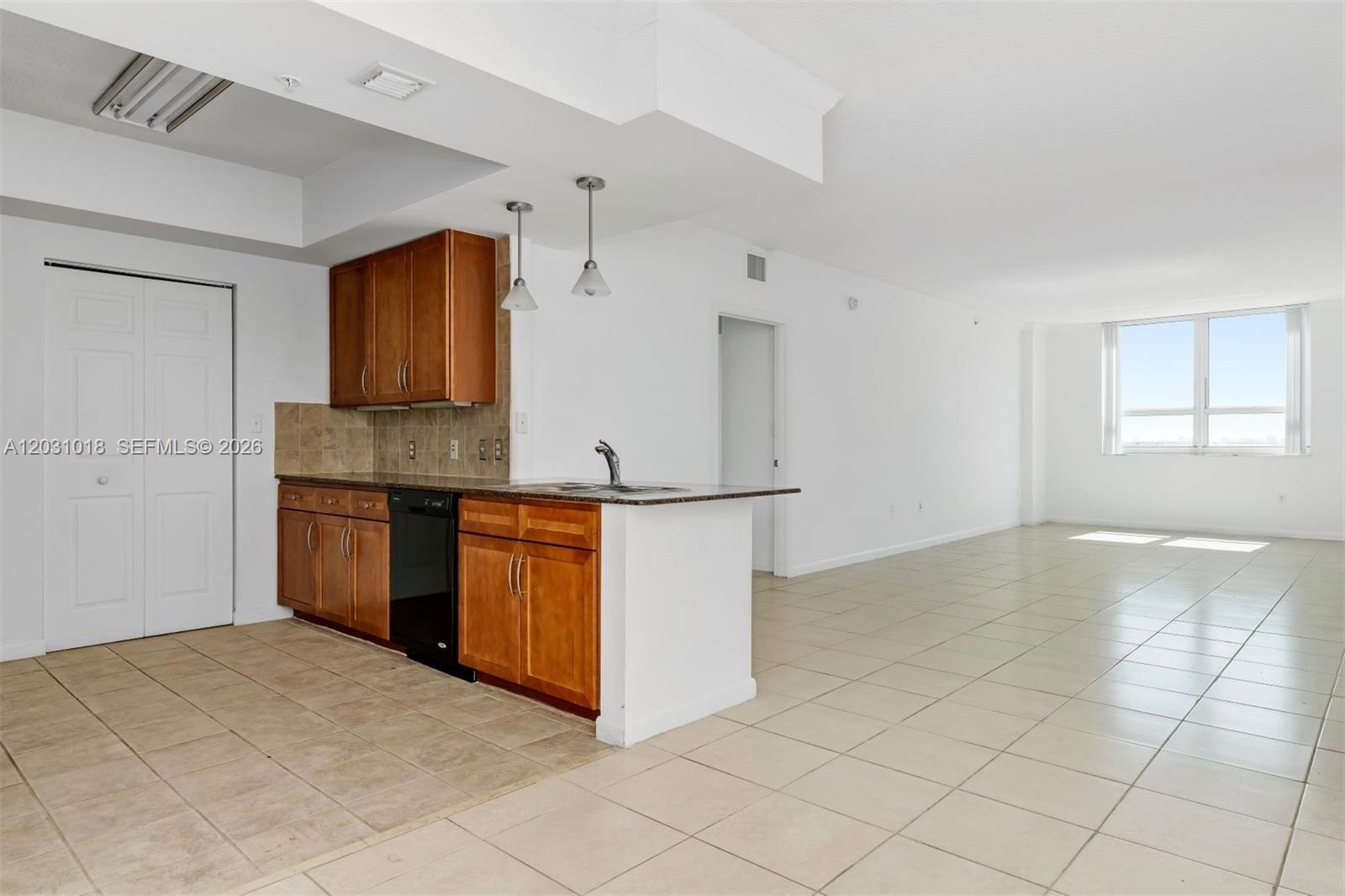 A kitchen with wood cabinets and a black dishwasher opens into a tiled living area — 2000 N Bayshore Dr # 420, Miami FL 33137, MIAMI, FL