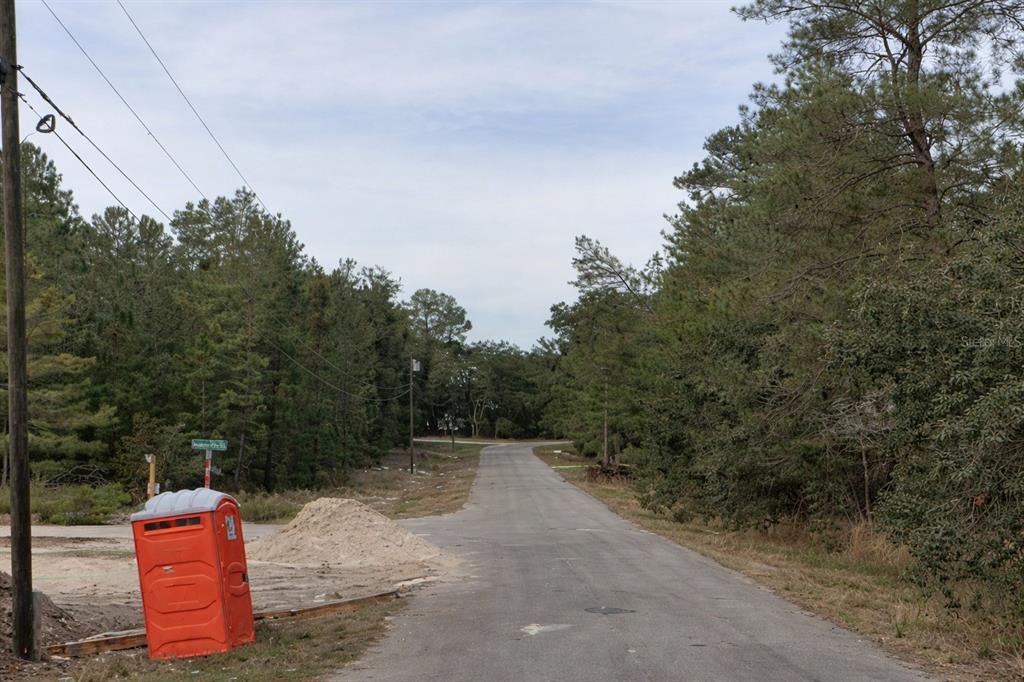 A paved road leads through a wooded area with a portable toilet on the left — MALAUKA PASS COURSE,, OCKLAWAHA, FL
