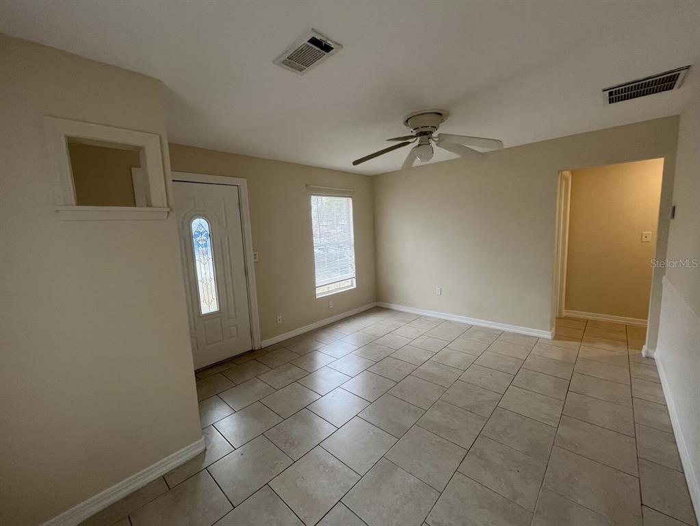 A living room with beige walls, tile flooring, a ceiling fan, and a front door — 2014 10TH STREET W, BRADENTON, FL