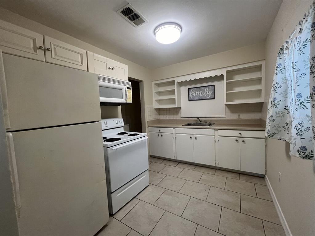 A kitchen features white cabinets, a white stove, a refrigerator, and light-colored tile flooring — 2014 10TH STREET W, BRADENTON, FL