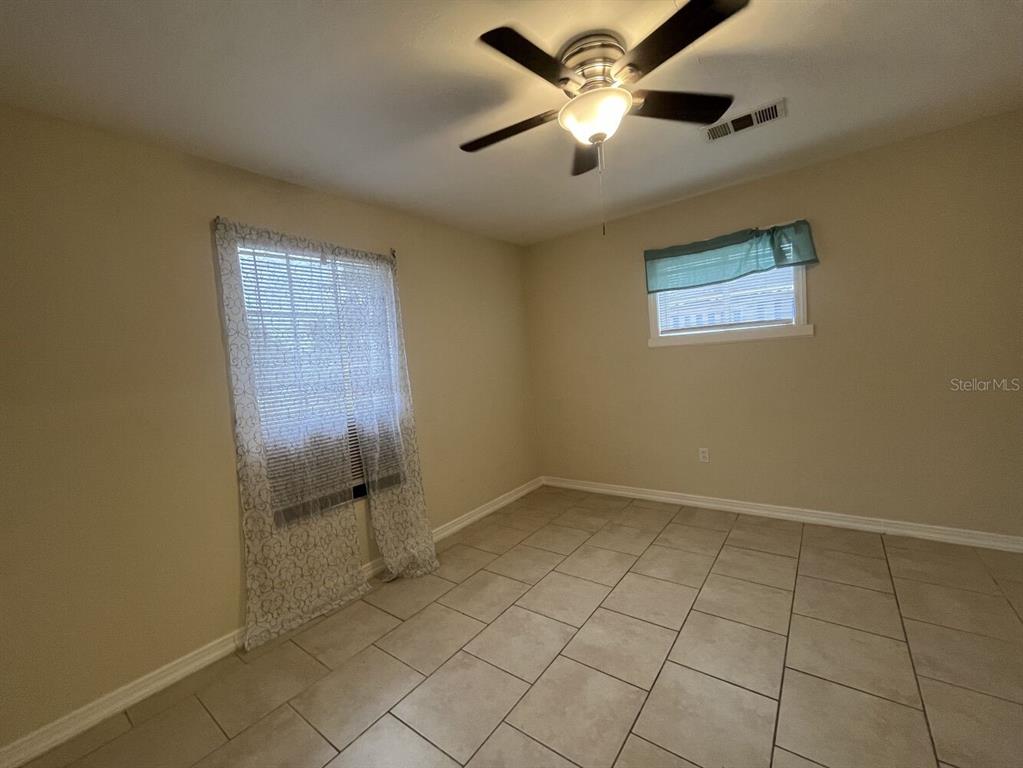 An empty room features beige walls, light-colored tile flooring, a ceiling fan, and two windows — 2014 10TH STREET W, BRADENTON, FL