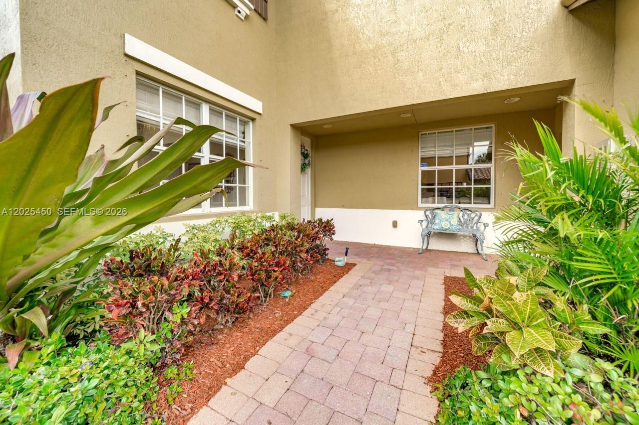 A paved walkway leads to a covered entryway with a bench and landscaped garden beds — 8345 NW 128th Ln # A, Parkland FL 33076, PARKLAND, FL