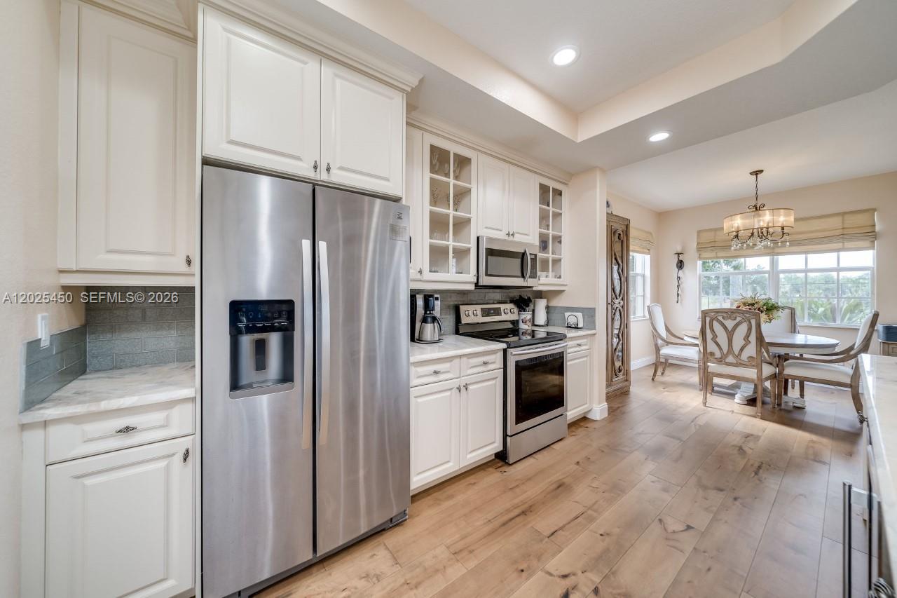 A kitchen features white cabinets, stainless steel appliances, and wood-look flooring near a dining area — 8345 NW 128th Ln # A, Parkland FL 33076, PARKLAND, FL