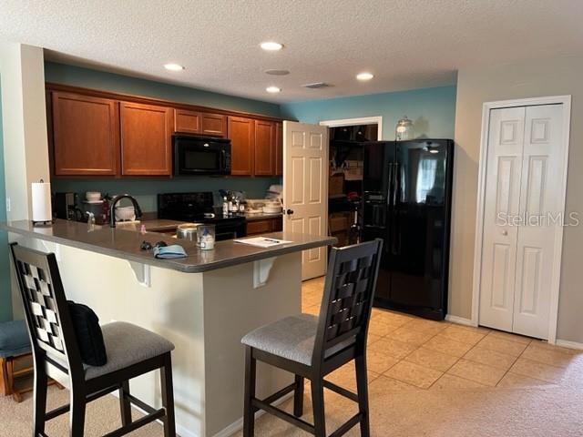A kitchen features wooden cabinets, a breakfast bar with two stools, and a black refrigerator — 523 MOUNT OLYMPUS BOULEVARD, NEW SMYRNA BEACH, FL