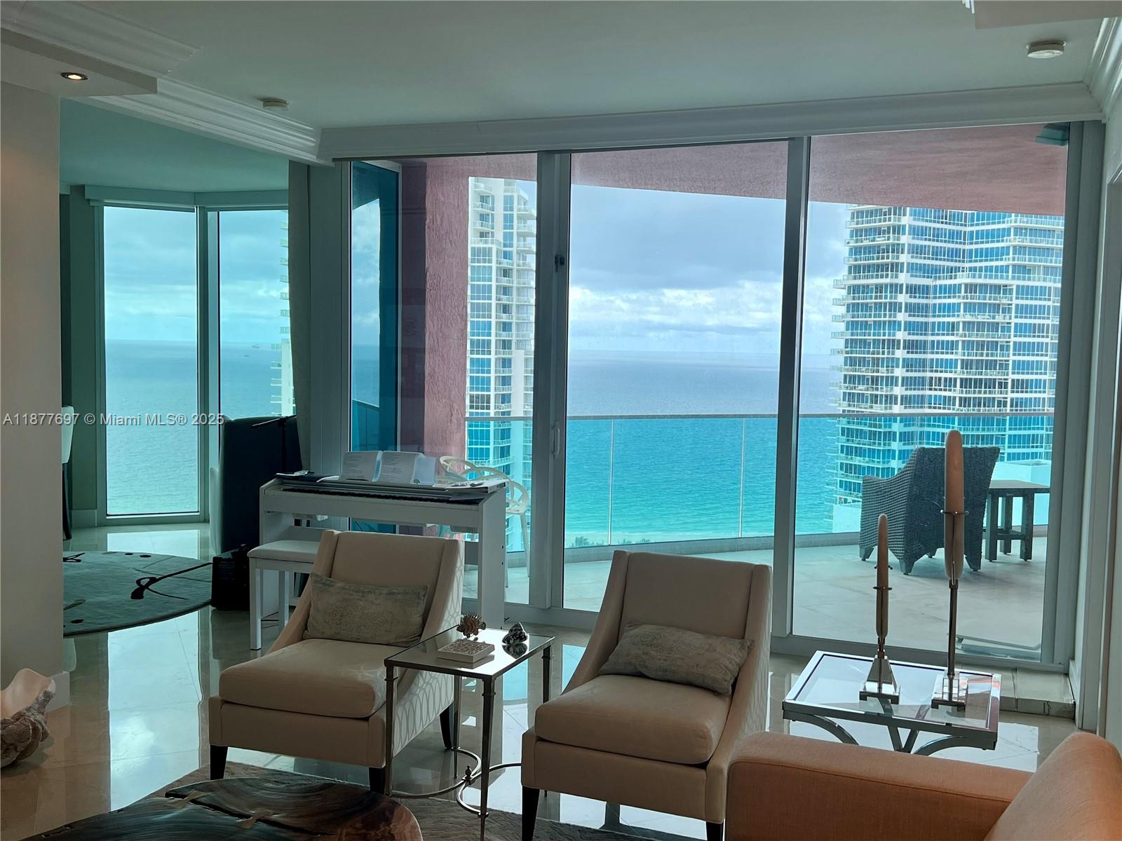 A living room features two armchairs, a white piano, and floor-to-ceiling windows overlooking the ocean — 300 S Pointe Dr # 2806, Miami Beach FL 33139, MIAMI BEACH, FL