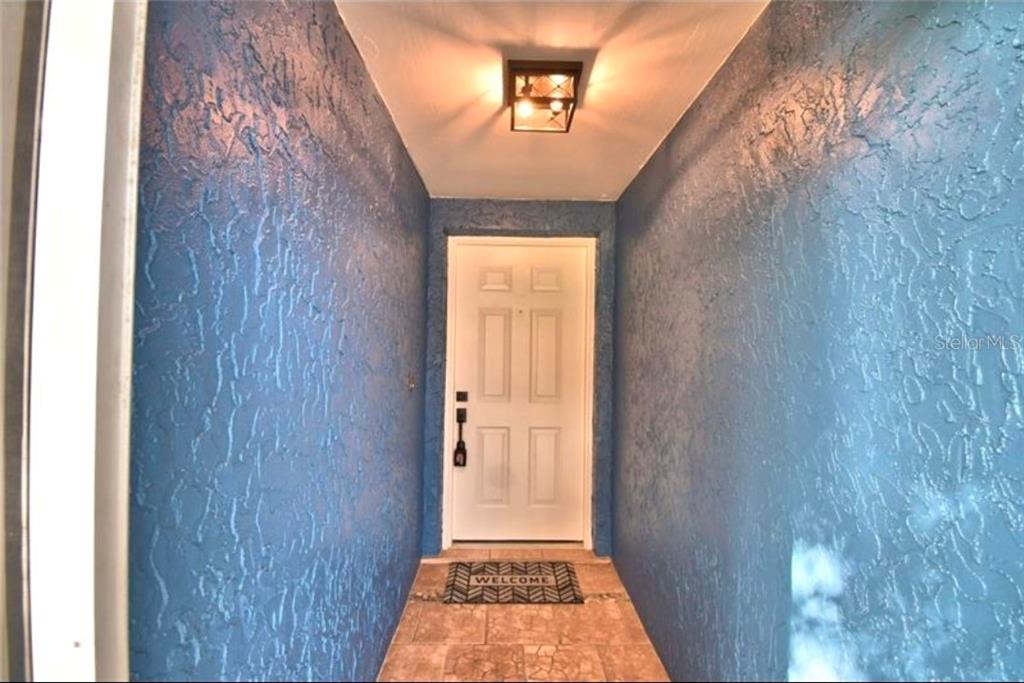 A covered entryway features blue textured walls, a white front door, and a tiled floor — 7504 WILLOW WISP DRIVE E, LAKELAND, FL