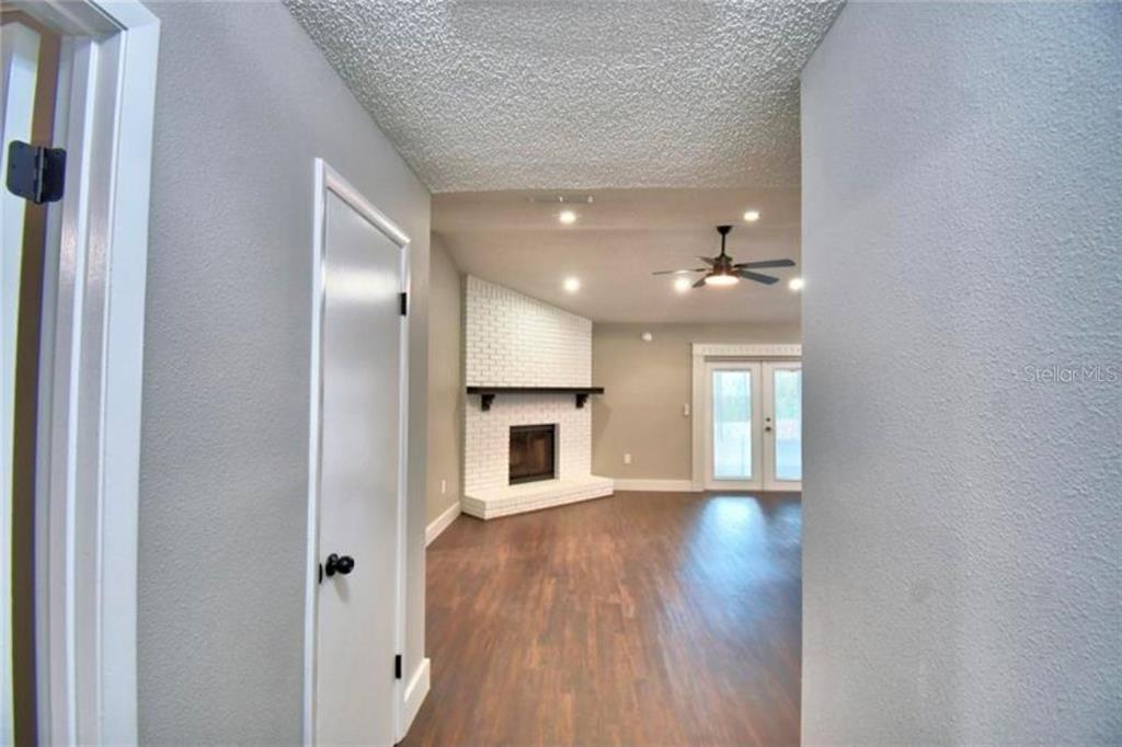 A view through a doorway into a living room with a white brick corner fireplace — 7504 WILLOW WISP DRIVE E, LAKELAND, FL