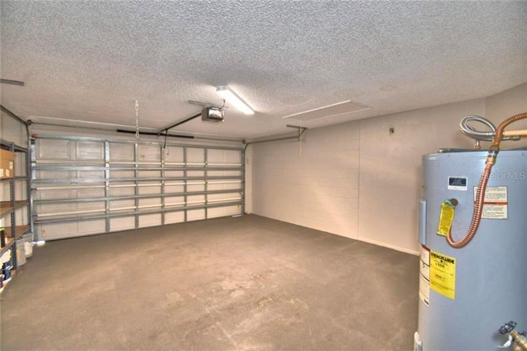A garage with a concrete floor, a white sectional door, and a water heater — 7504 WILLOW WISP DRIVE E, LAKELAND, FL