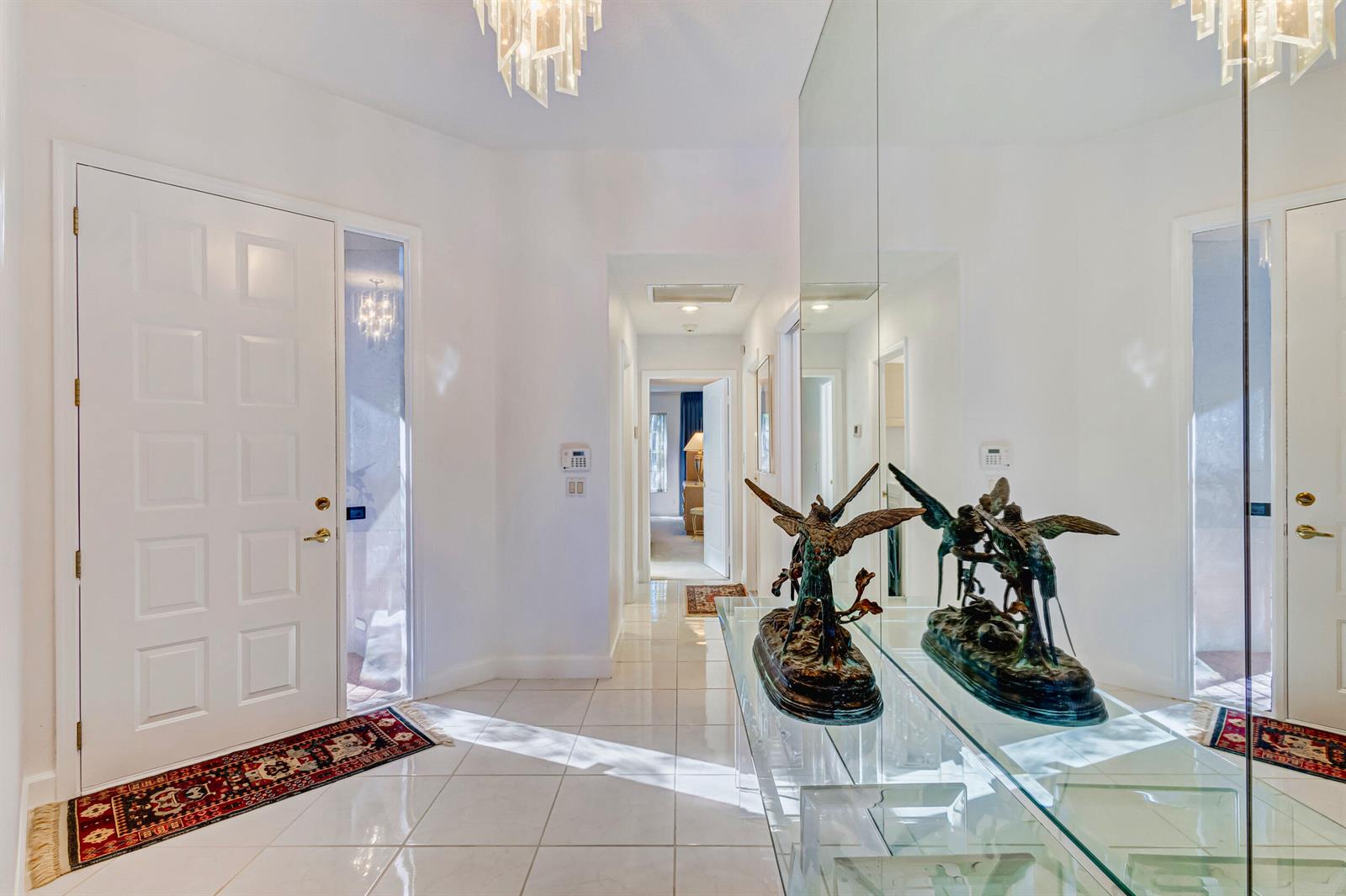 A bright entryway features white tile floors, a mirrored wall, and a decorative bronze sculpture — 919 Augusta Pointe Drive, Palm Beach Gardens FL 33418, PALM BEACH GARDENS, FL