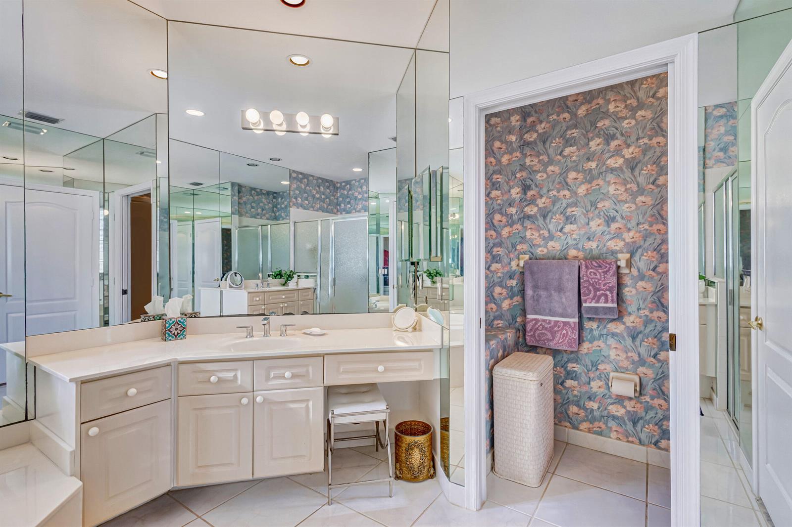 A bathroom features a vanity with a mirror, floral wallpaper, and a separate toilet area — 919 Augusta Pointe Drive, Palm Beach Gardens FL 33418, PALM BEACH GARDENS, FL