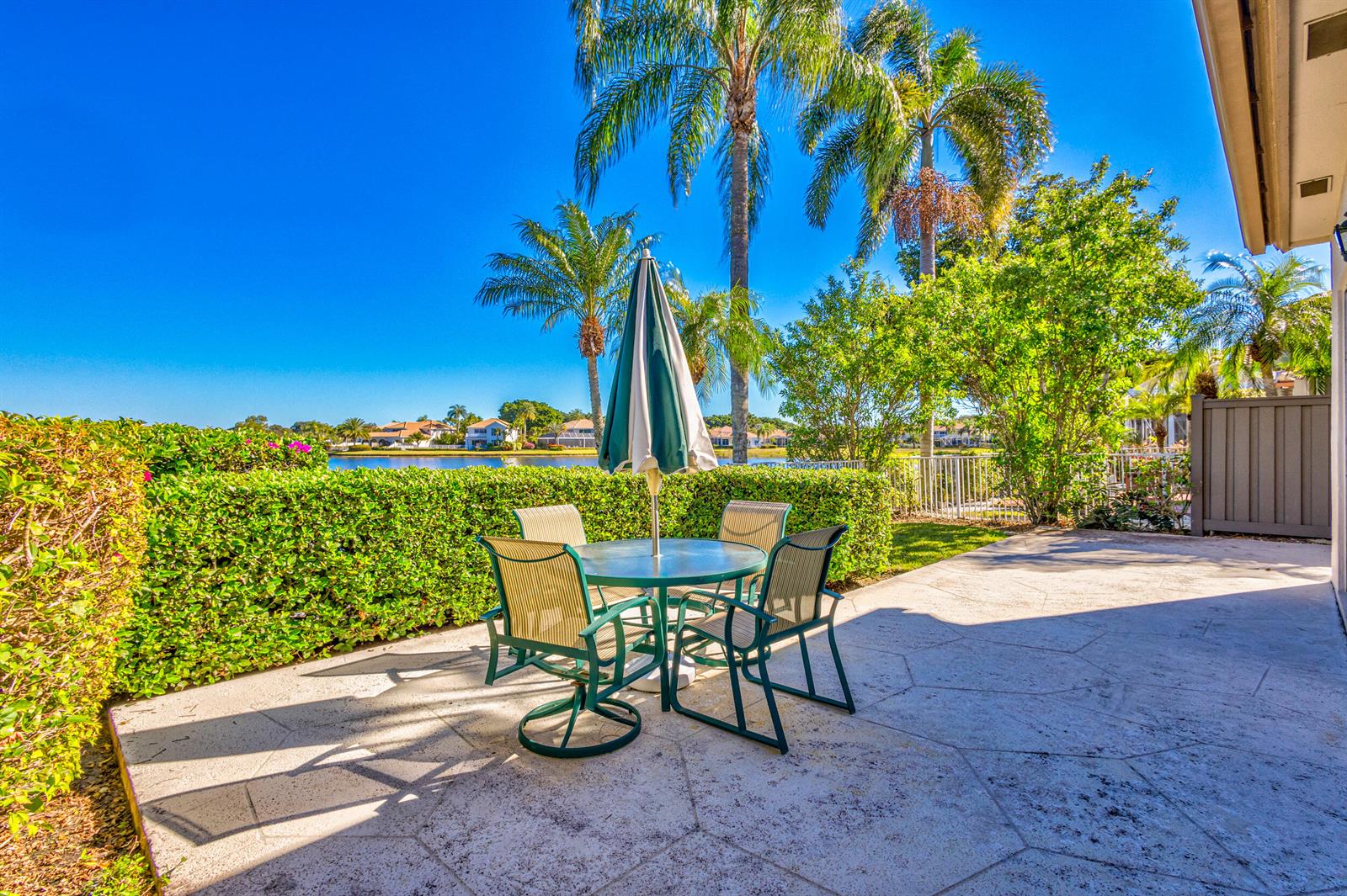 A patio with a dining set and umbrella overlooks a lake and palm trees — 919 Augusta Pointe Drive, Palm Beach Gardens FL 33418, PALM BEACH GARDENS, FL