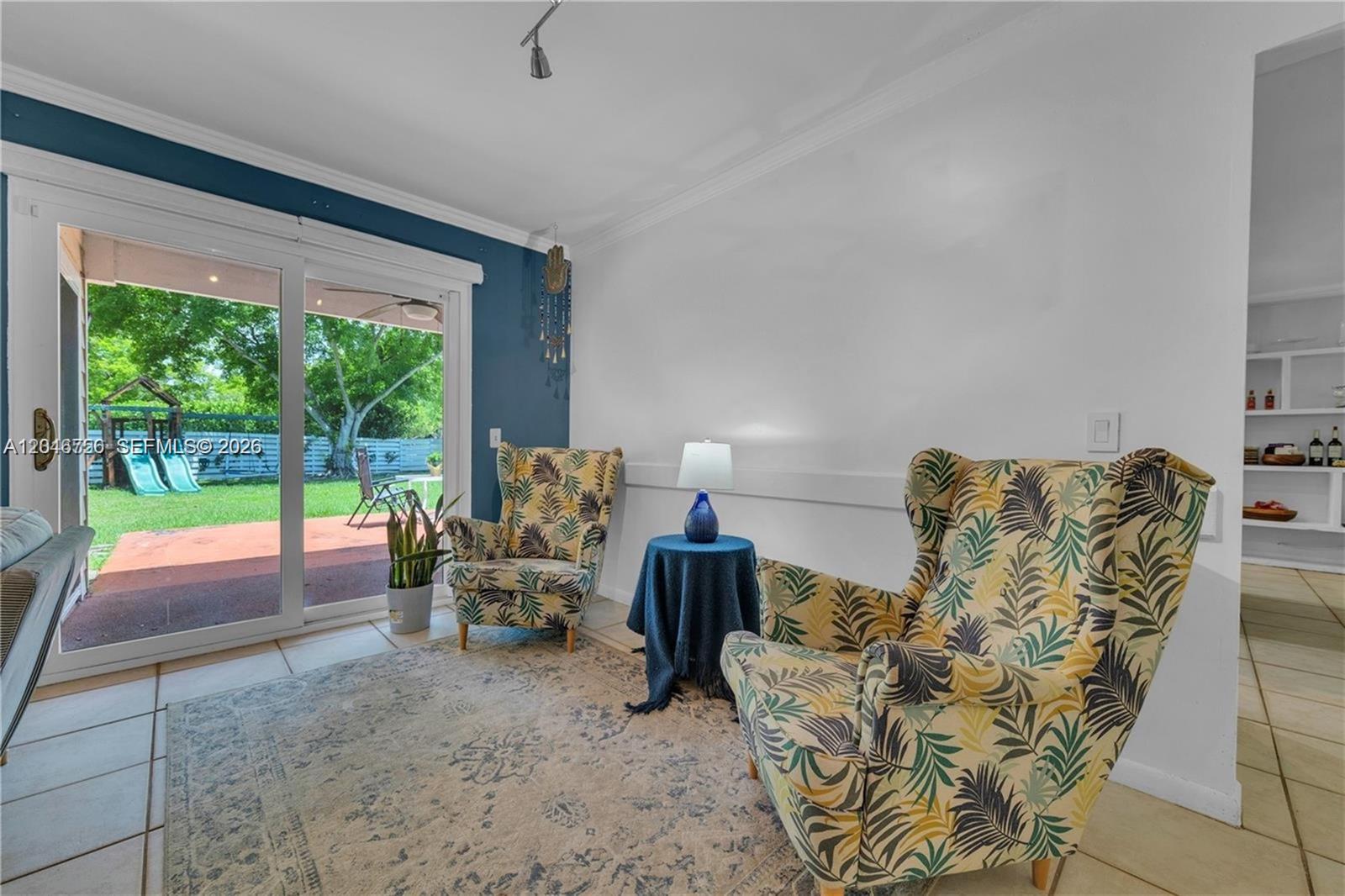 A sunlit living area features two patterned armchairs, a small side table, and sliding glass doors — 14630 SW 147th Ct, Miami FL 33196, MIAMI, FL