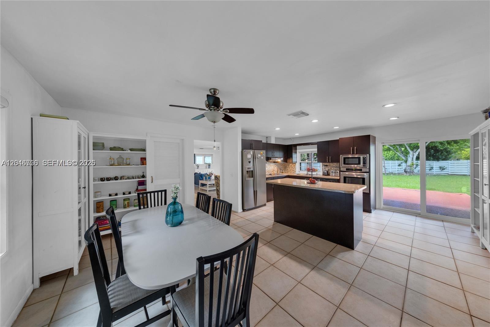 A dining area with a white table and black chairs opens into a modern kitchen — 14630 SW 147th Ct, Miami FL 33196, MIAMI, FL