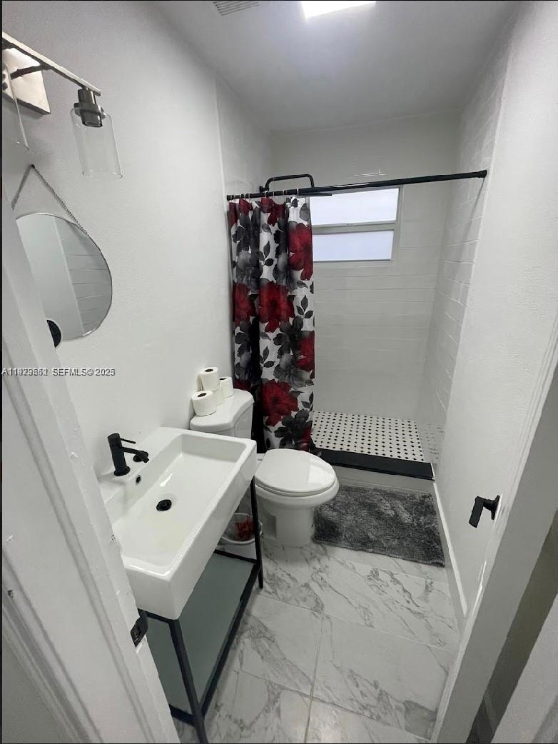 A small bathroom features a pedestal sink, a toilet, and a walk-in shower with curtains — 3085 NW 51st St, Miami FL 33142, MIAMI, FL