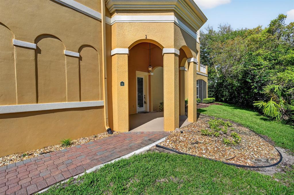A yellow stucco building features an arched entryway with a brick walkway and landscaping — 40 CASA BELLA CIRCLE UNIT 1101, PALM COAST, FL
