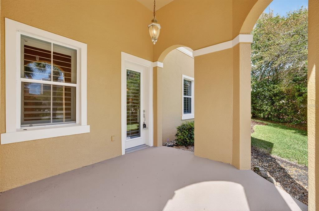 A covered patio features tan stucco walls, a hanging light fixture, and a glass door — 40 CASA BELLA CIRCLE UNIT 1101, PALM COAST, FL