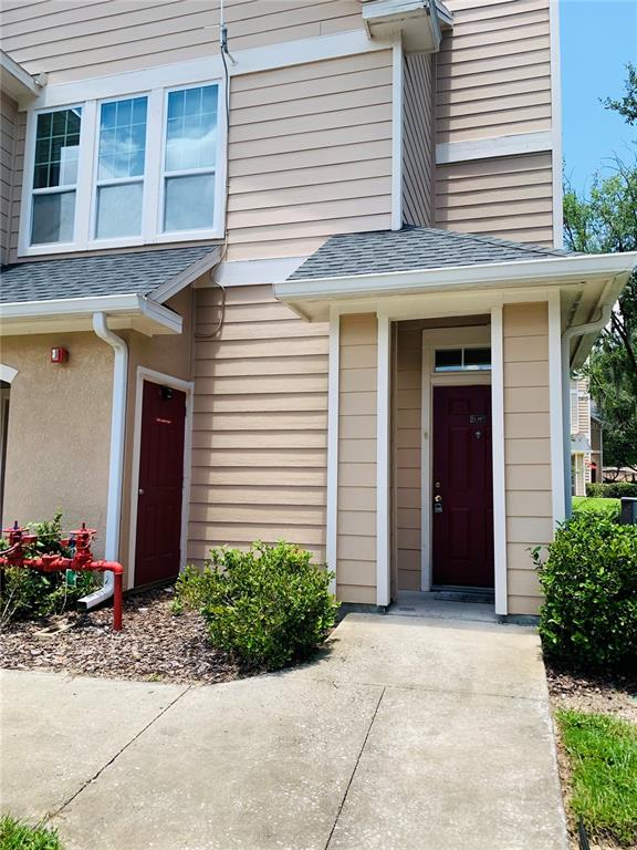 Exterior view of a two-story building with beige siding, two red doors, and landscaping — 1980 ERVING CIRCLE UNIT 107, OCOEE, FL