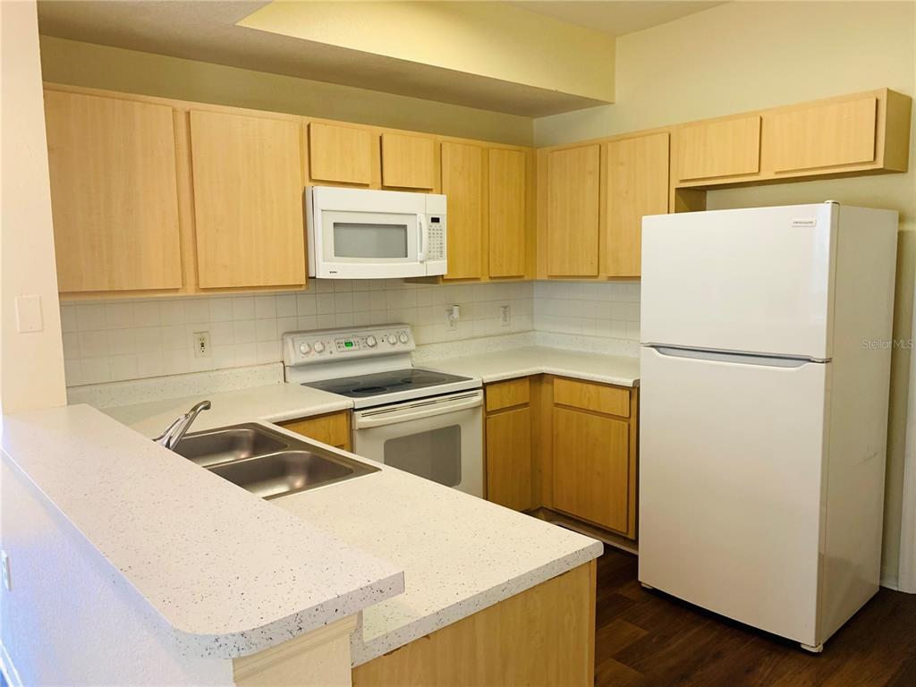 A kitchen features light wood cabinets, white appliances, and a speckled countertop with a sink — 1980 ERVING CIRCLE UNIT 107, OCOEE, FL