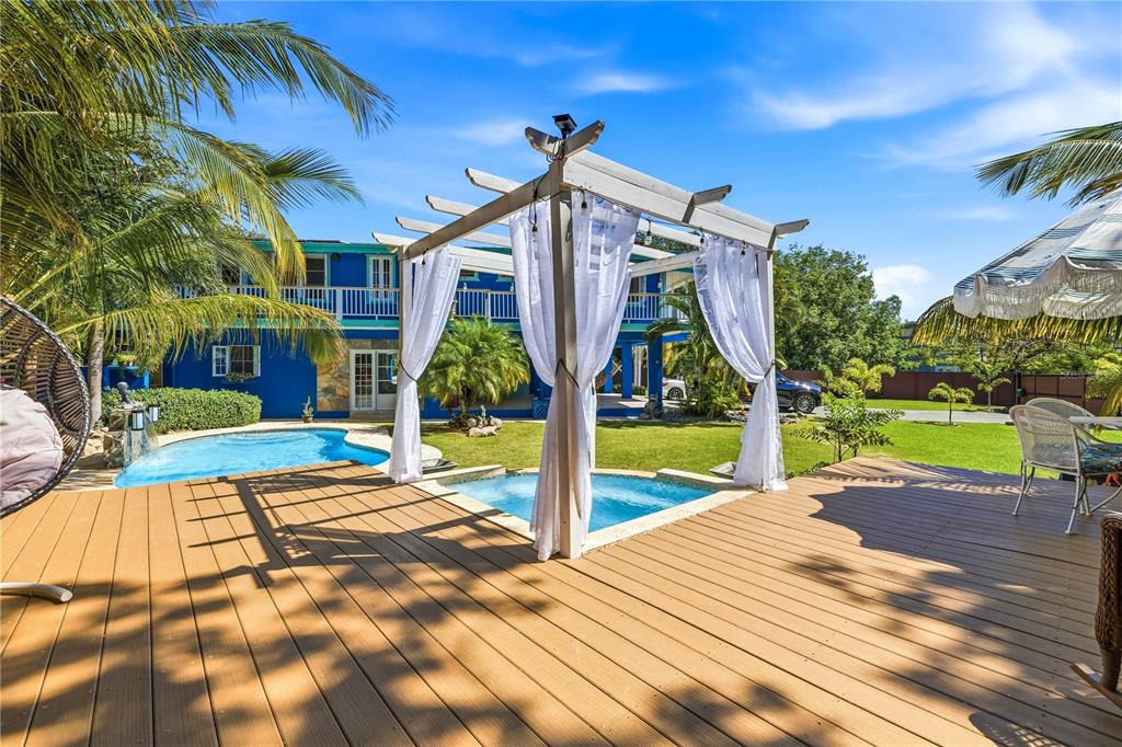 A wooden deck features a white pergola with curtains overlooking a pool and blue house — 1/1A GIL BOUYET STREET, CABO ROJO, PR