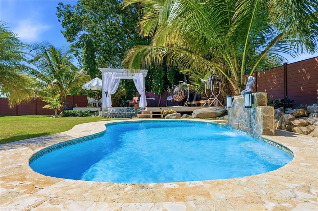 A backyard swimming pool features a stone waterfall, a wooden deck, and a white pergola — 1/1A GIL BOUYET STREET, CABO ROJO, PR