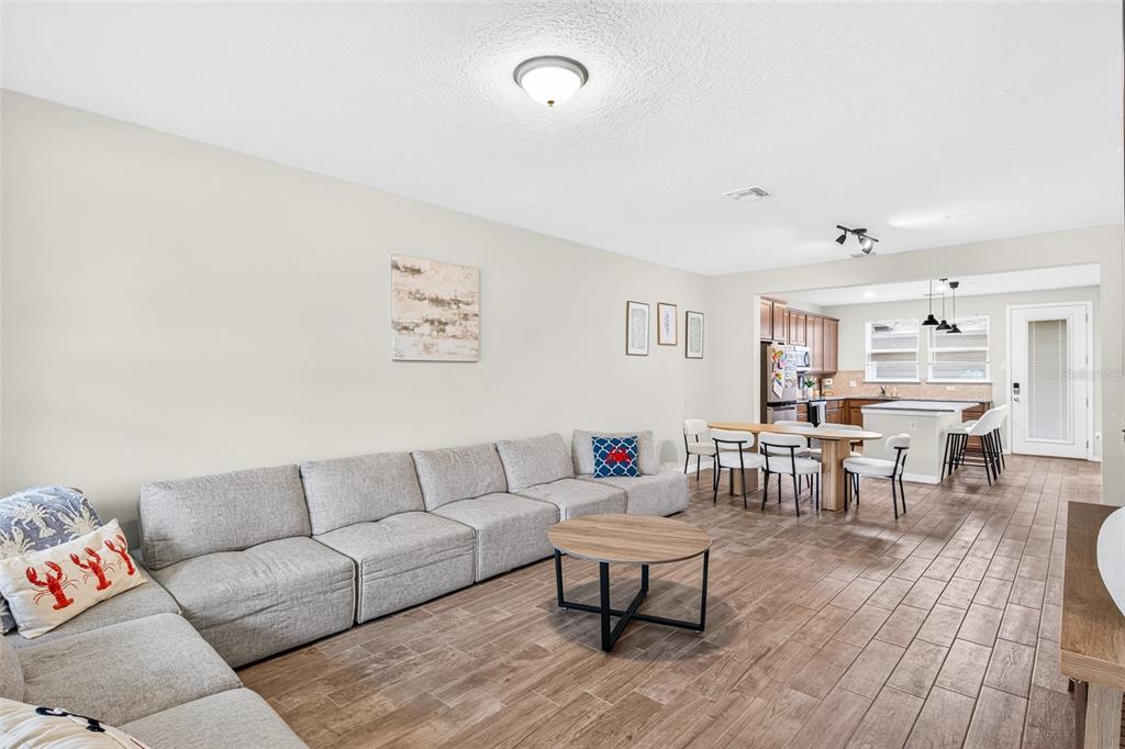 A living room with a large gray sectional sofa, wood-look tile flooring, and an open kitchen — 5133 SAPLING SPROUT DRIVE, ORLANDO, FL