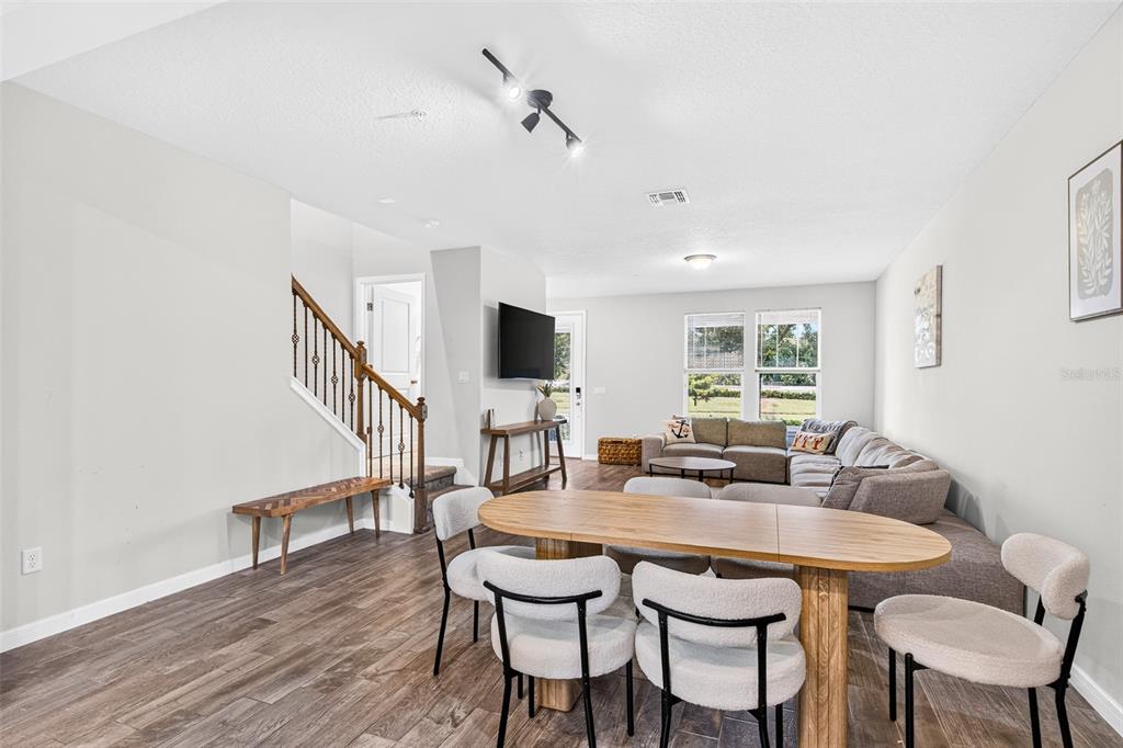 A living and dining area with wood-look flooring, a staircase, and a large sectional sofa — 5133 SAPLING SPROUT DRIVE, ORLANDO, FL