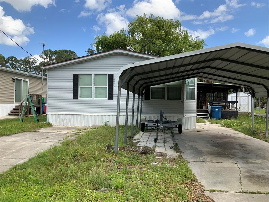 A light-gray mobile home features a metal carport and a concrete driveway under a blue sky — 1639 BASS AVENUE, SEVILLE, FL