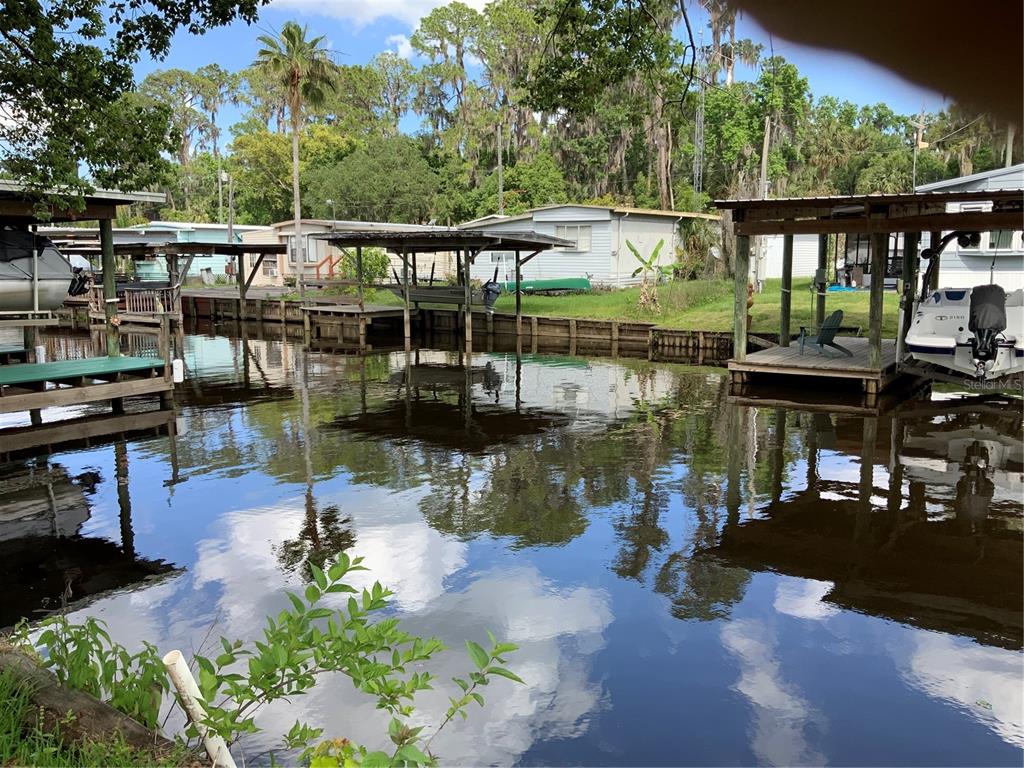 A canal view featuring boat docks, covered boat slips, and mobile homes in the background — 1639 BASS AVENUE, SEVILLE, FL