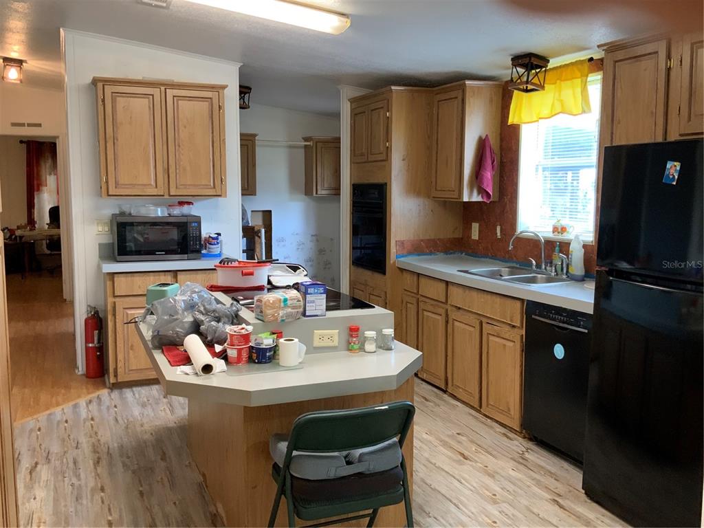 A kitchen with wood cabinets, a central island, black appliances, and light-colored wood-look flooring — 1639 BASS AVENUE, SEVILLE, FL