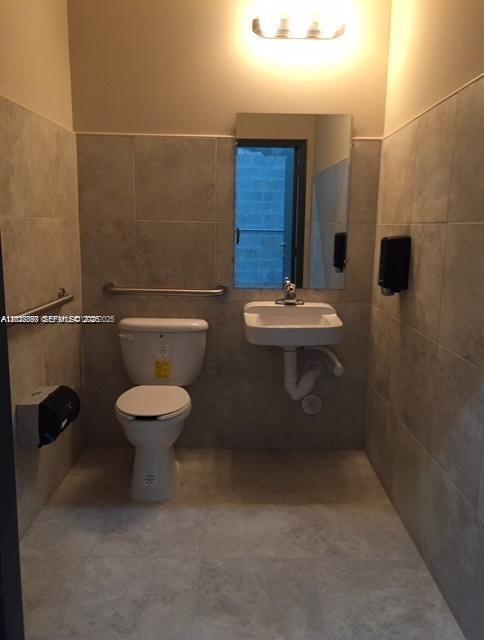 A small, tiled accessible restroom features a white toilet, a wall-mounted sink, and a mirror — 2188 NW 26th Ave, Miami FL 33142, MIAMI, FL