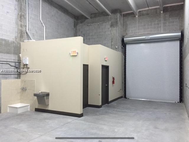 An industrial warehouse interior features a concrete floor, a roll-up door, and two small rooms — 2188 NW 26th Ave, Miami FL 33142, MIAMI, FL